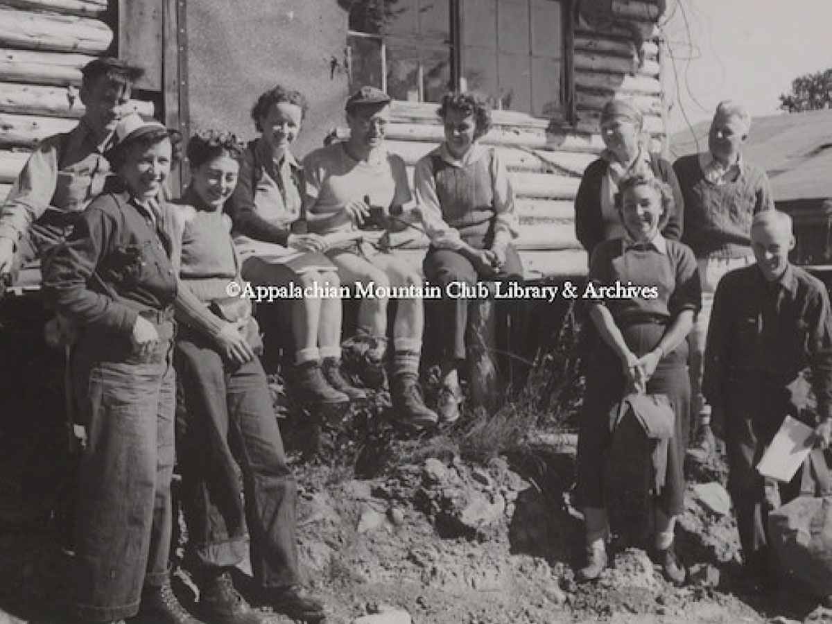 Hikers sitting and standing beside a logging camp cabin