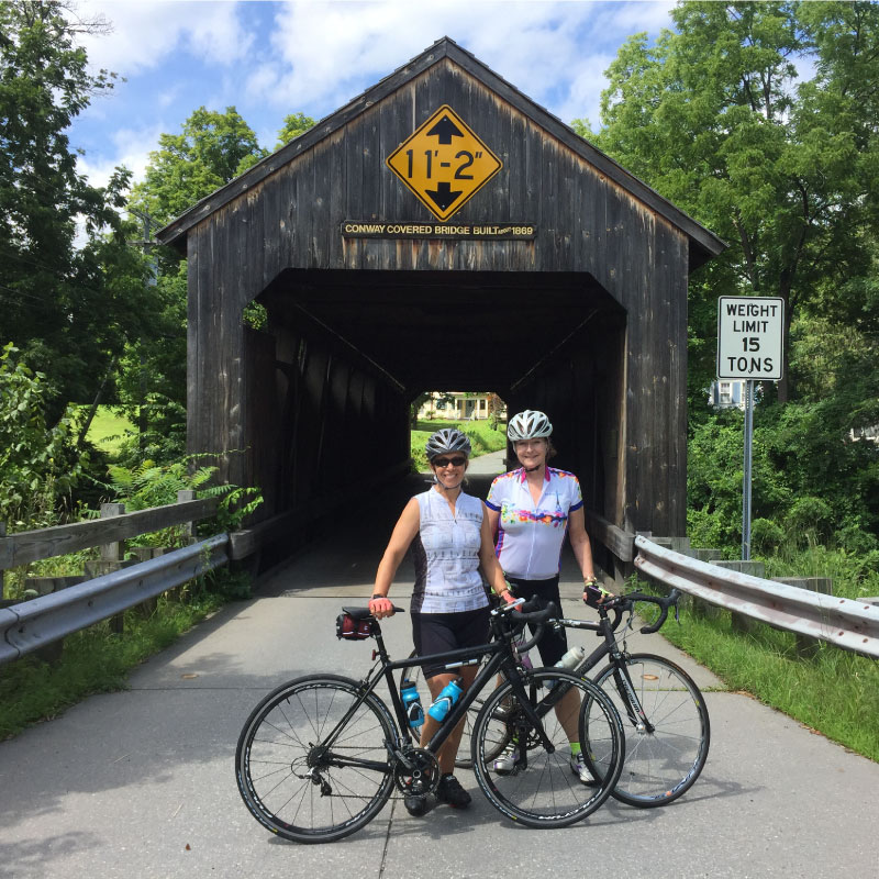 Cyclists pose in front of a covered bridge