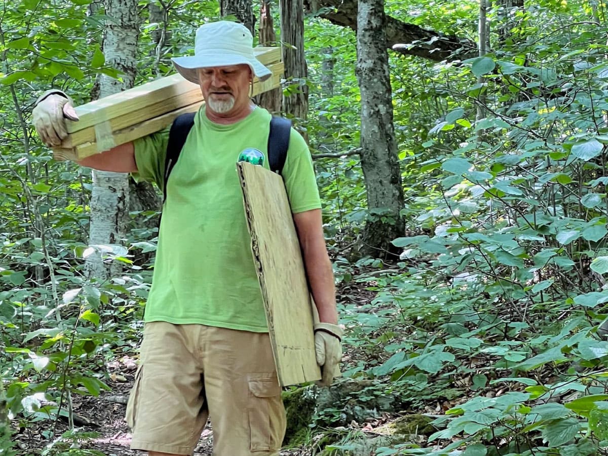 A worker carrying lumber for the Mt Greylock privy repair