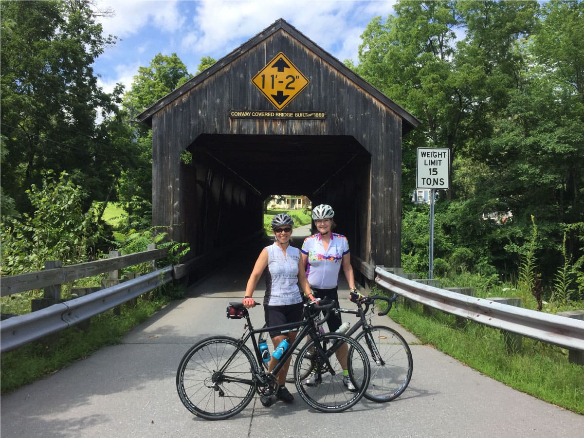 Two cyclists stand before a covered bridge