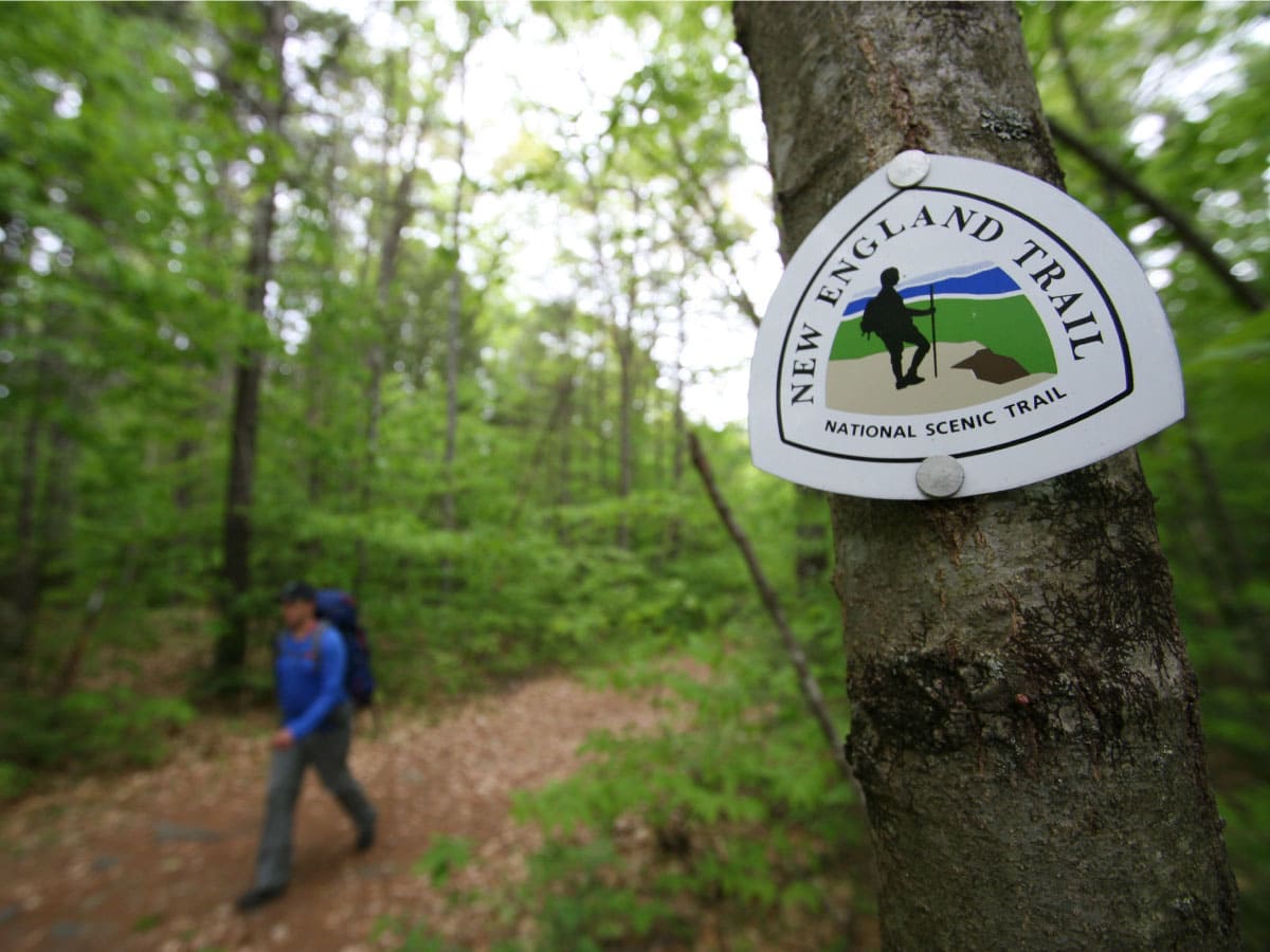 A hiker walks past a NET trail sign