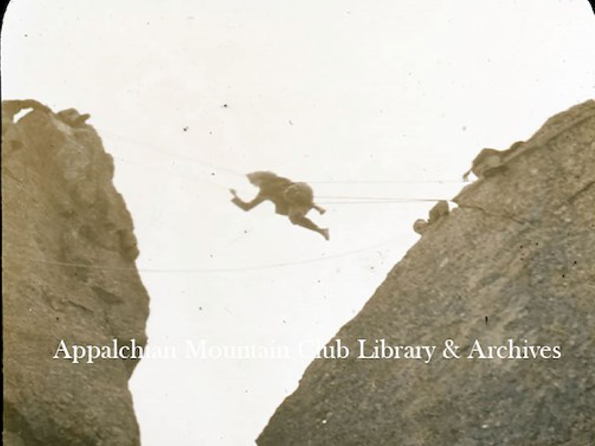 Miriam Underhill crossing a chasm between two rock faces on ropes